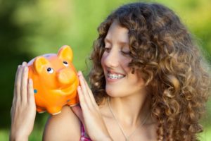 Woman with braces in Hopkinton holding piggy bank and smiling 