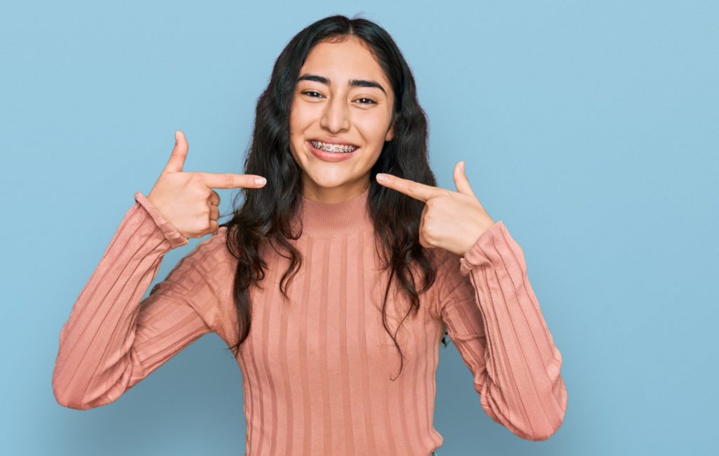 Girl with braces smiling while pointing to her teeth